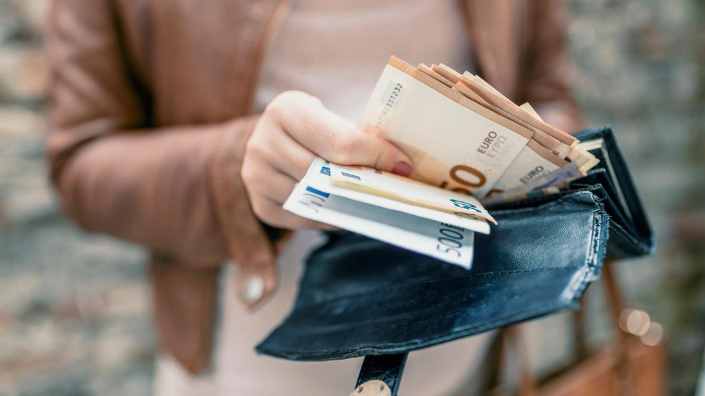 Frau zieht ein Bündel von Geldscheinen aus ihrer Brieftasche.