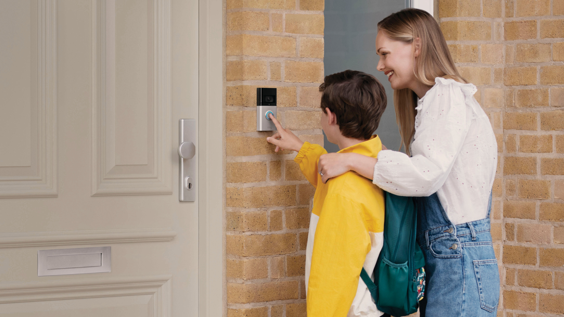 Eine Frau und ein Junge stehen vor einer Haustür, neben der eine Video Doorbell 4 von Ring installiert ist.