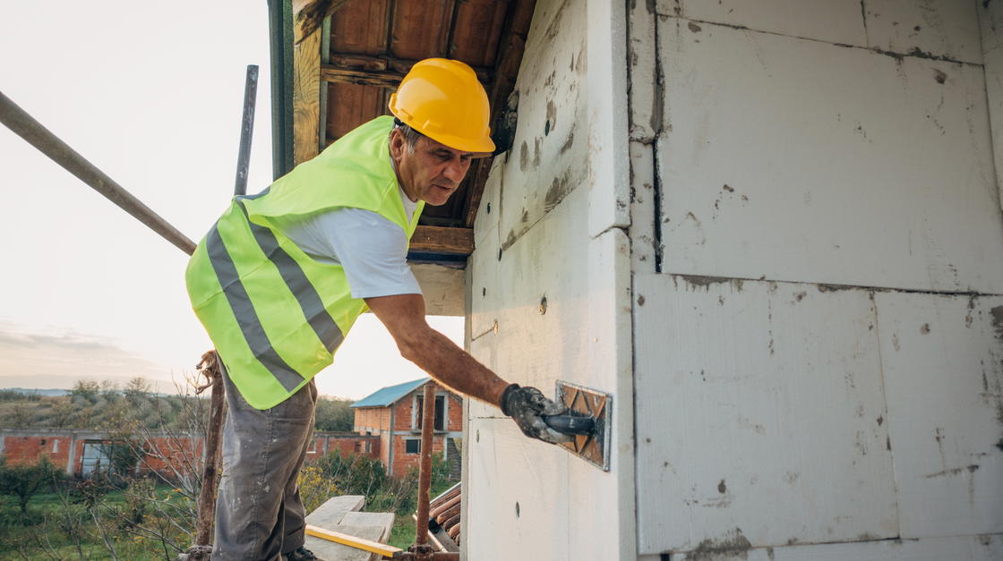 Ein Bauarbeiter saniert und dämmt die Fassade eines Hauses.