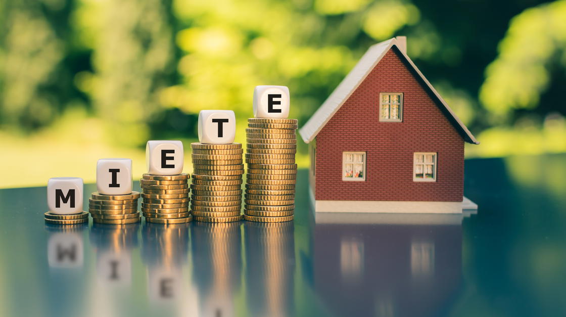 Miniaturhaus mit größer werdenden Münzstapeln, auf denen einzelne Buchstaben das Wort "Miete" bilden