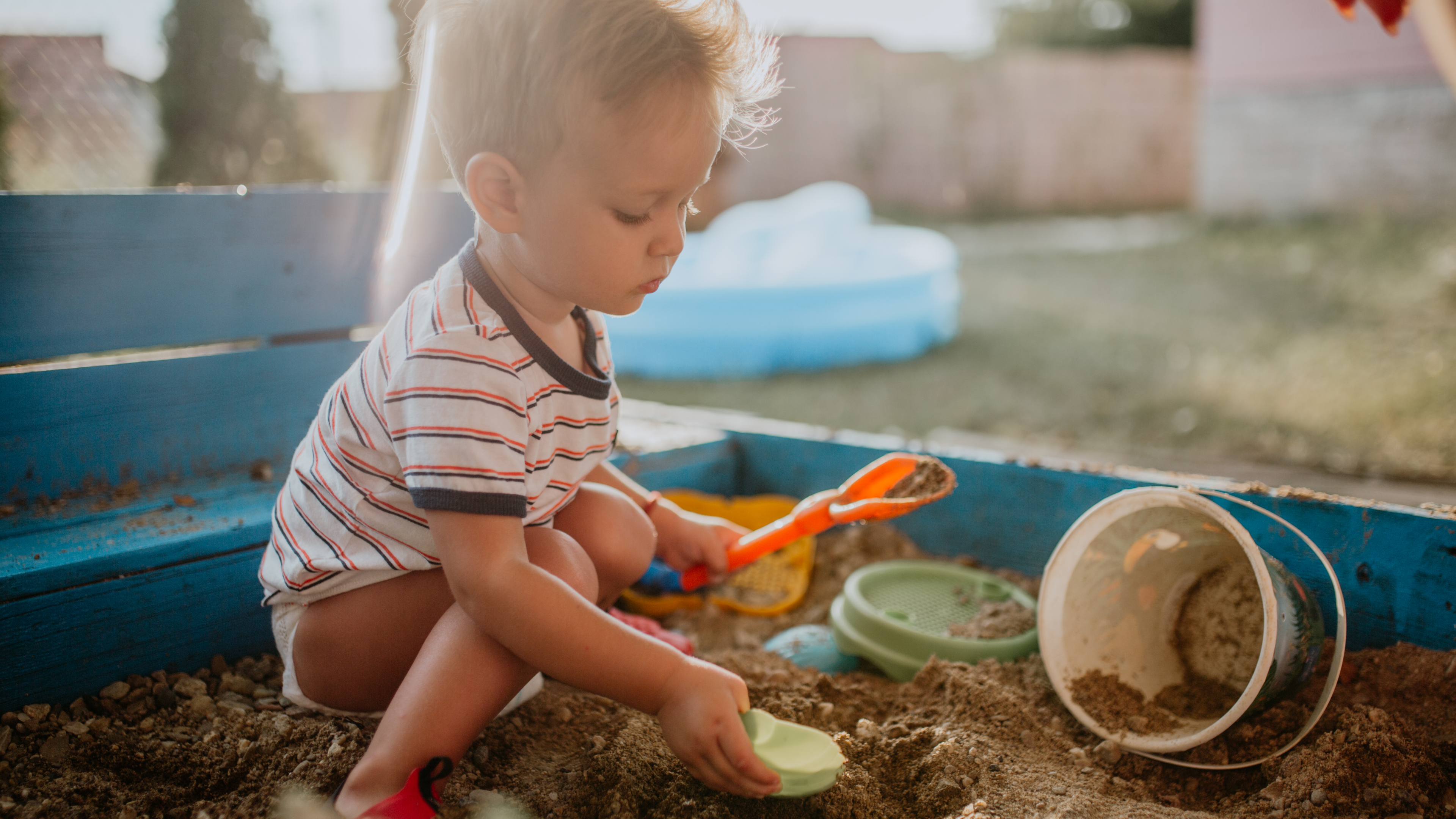 Ein Kind spielt mit seinen Spielzeugen im Sandkasten.