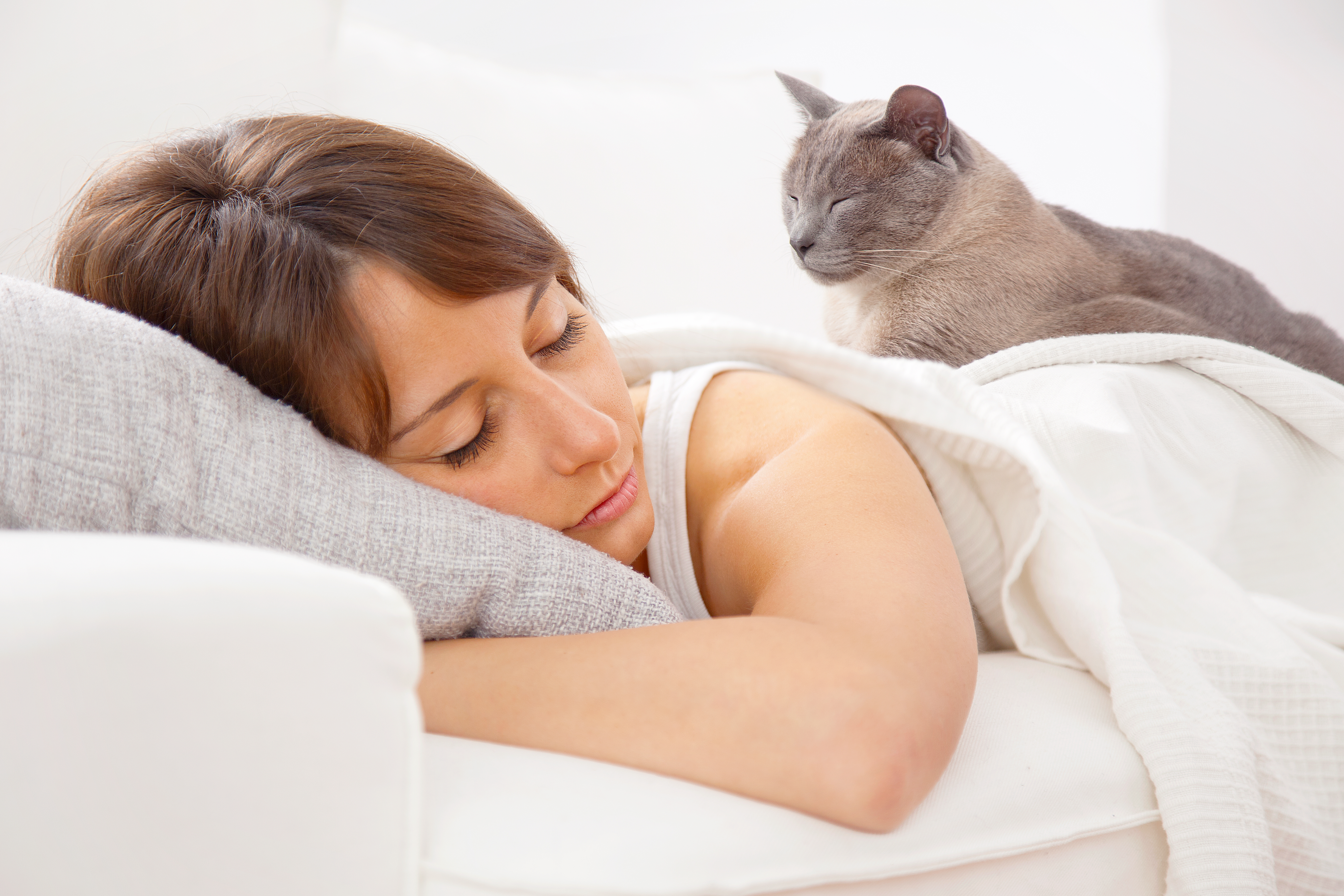 Frau schläft mit Katze im Bett