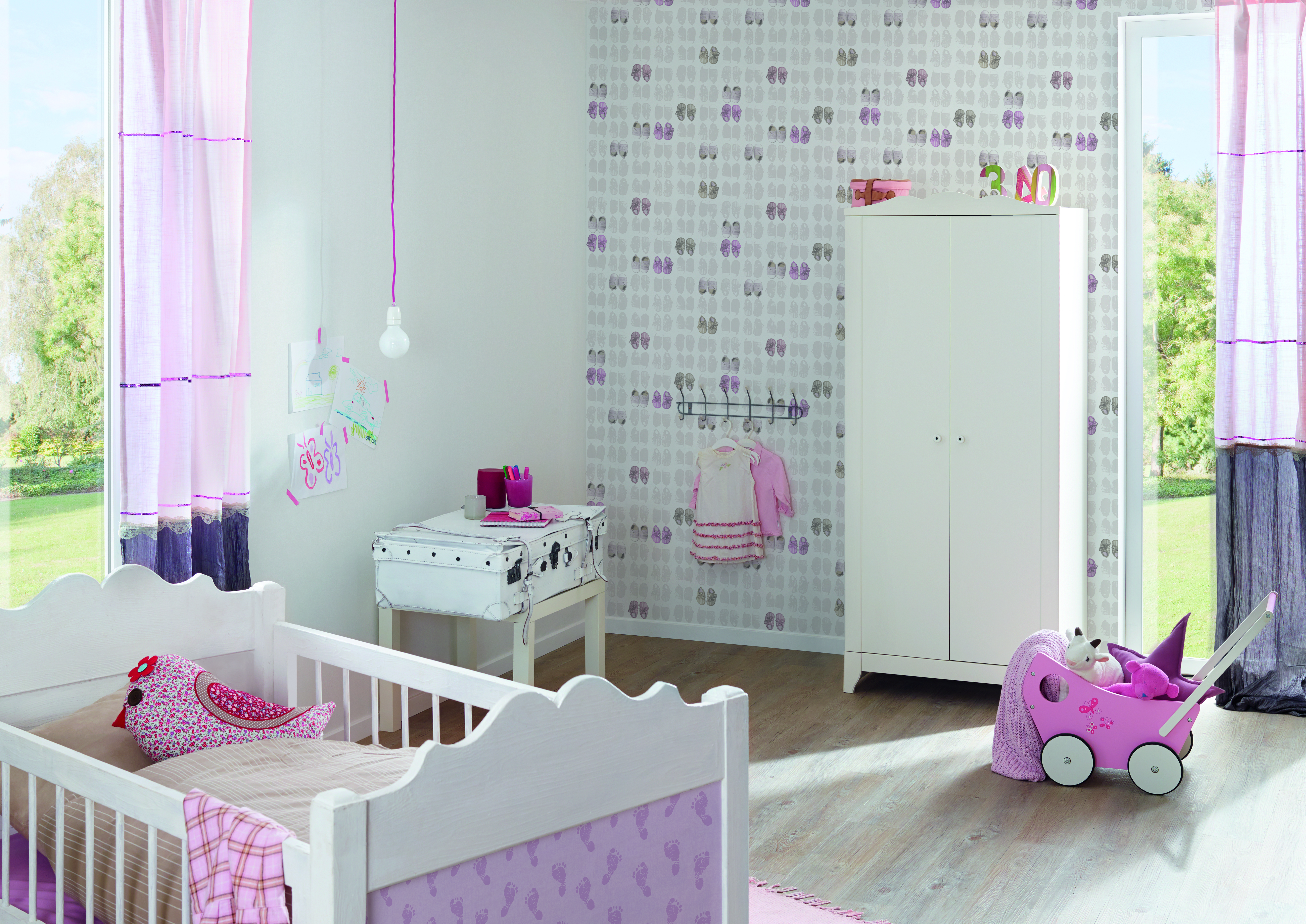 Babyzimmer mit Gitterbett und Kleiderschrank vor grafischer Tapete.