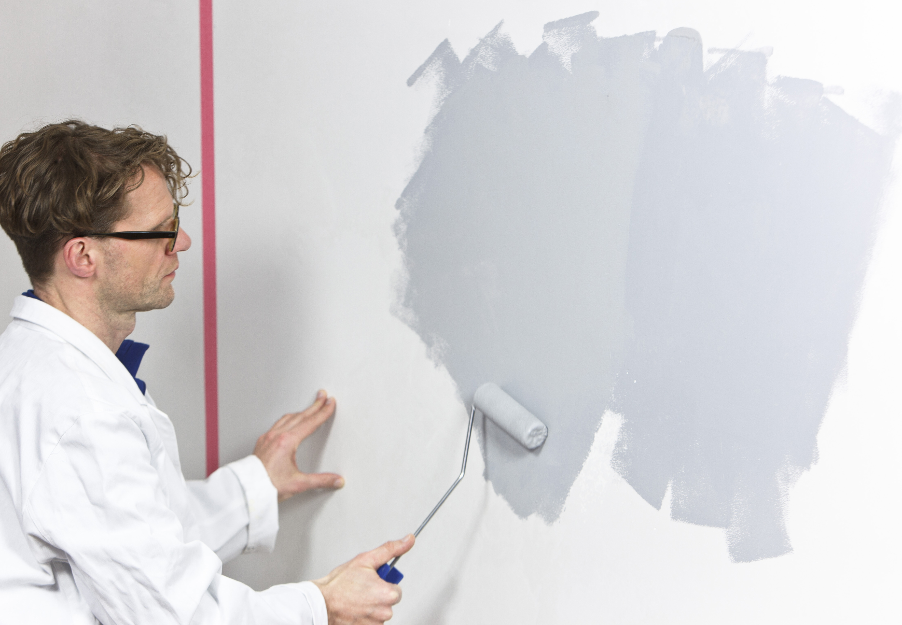 Mann rollt mit Malerrolle grauen Putz an die Wand