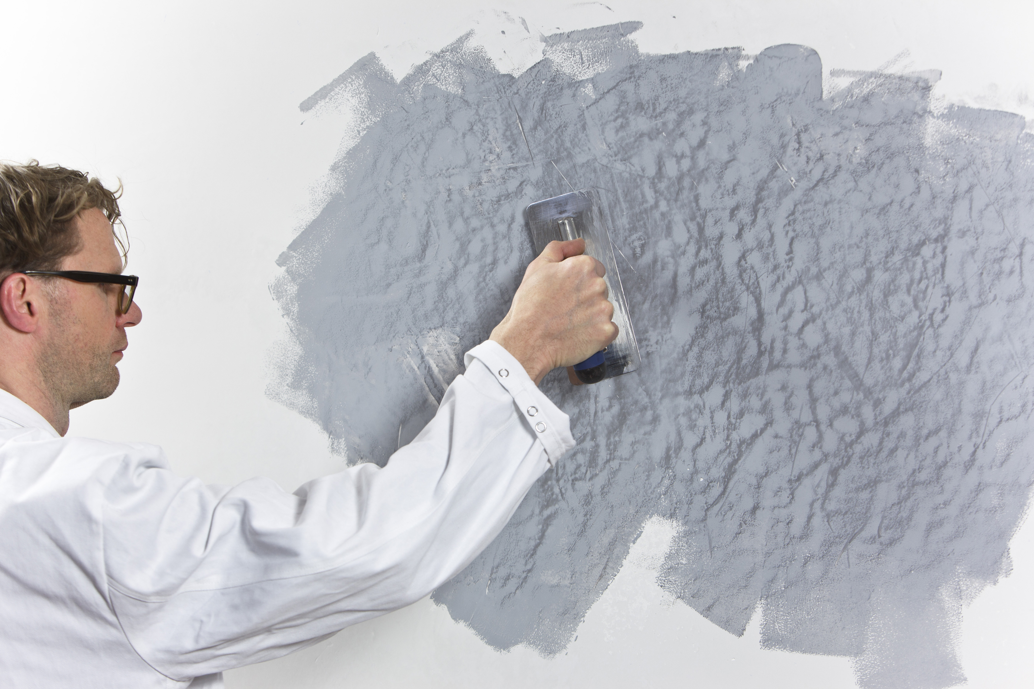 Mann spachtelt grauen Putz an die Wand