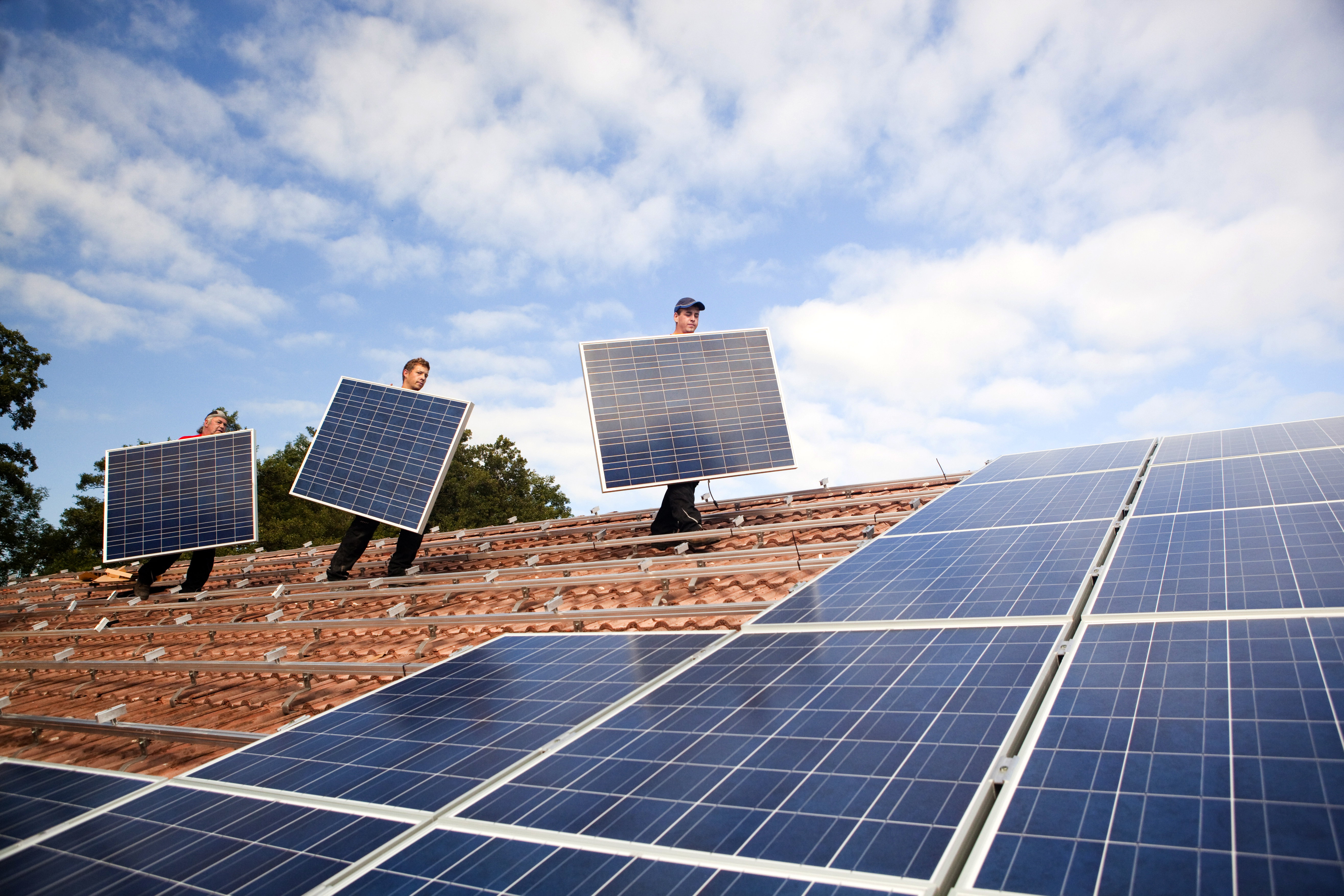 Drei Männer installieren eine Photovoltaikanlage auf einem Dach