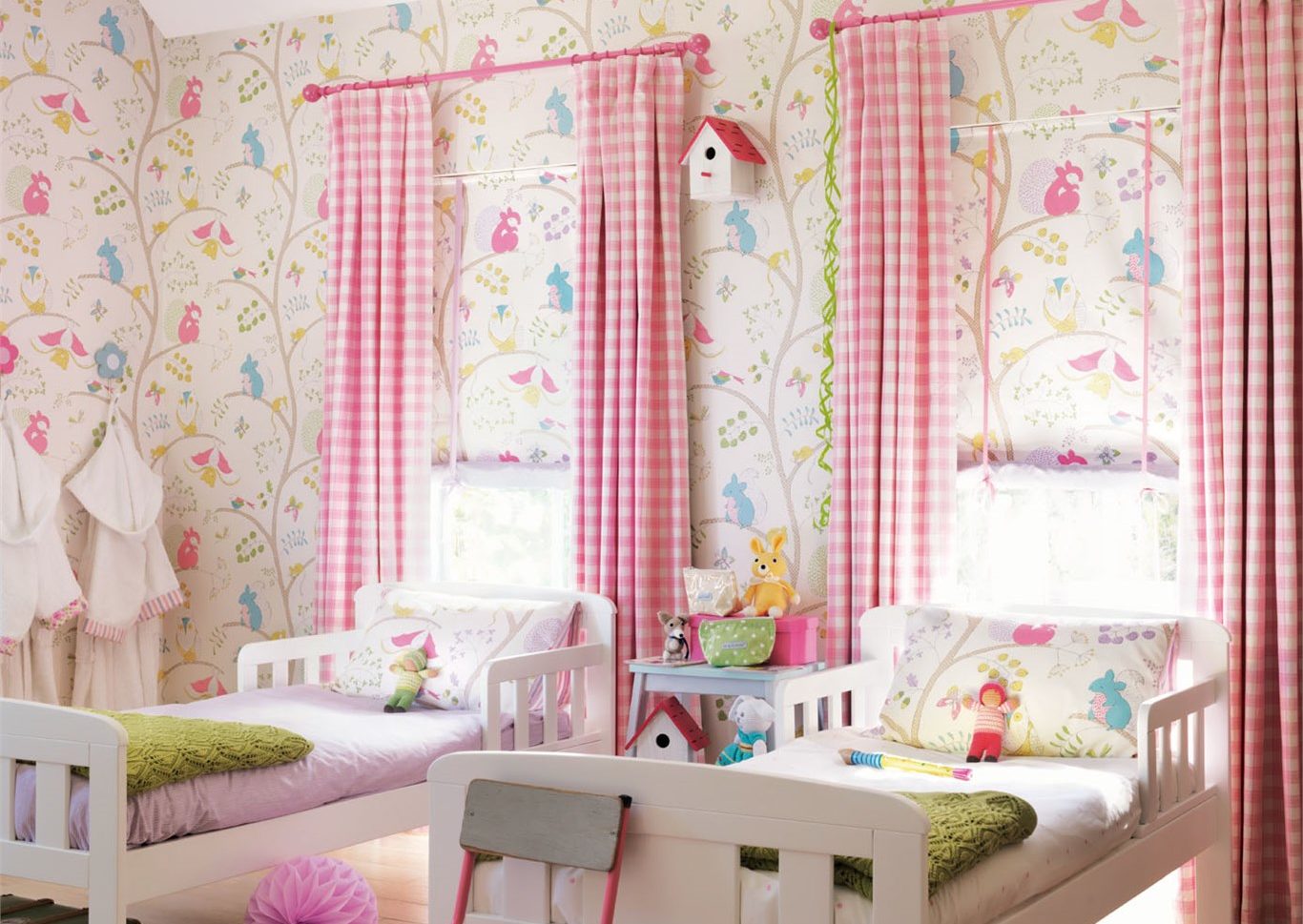 Zwei Kinderbetten stehen vor zwei Fenster und bunter Tapete.