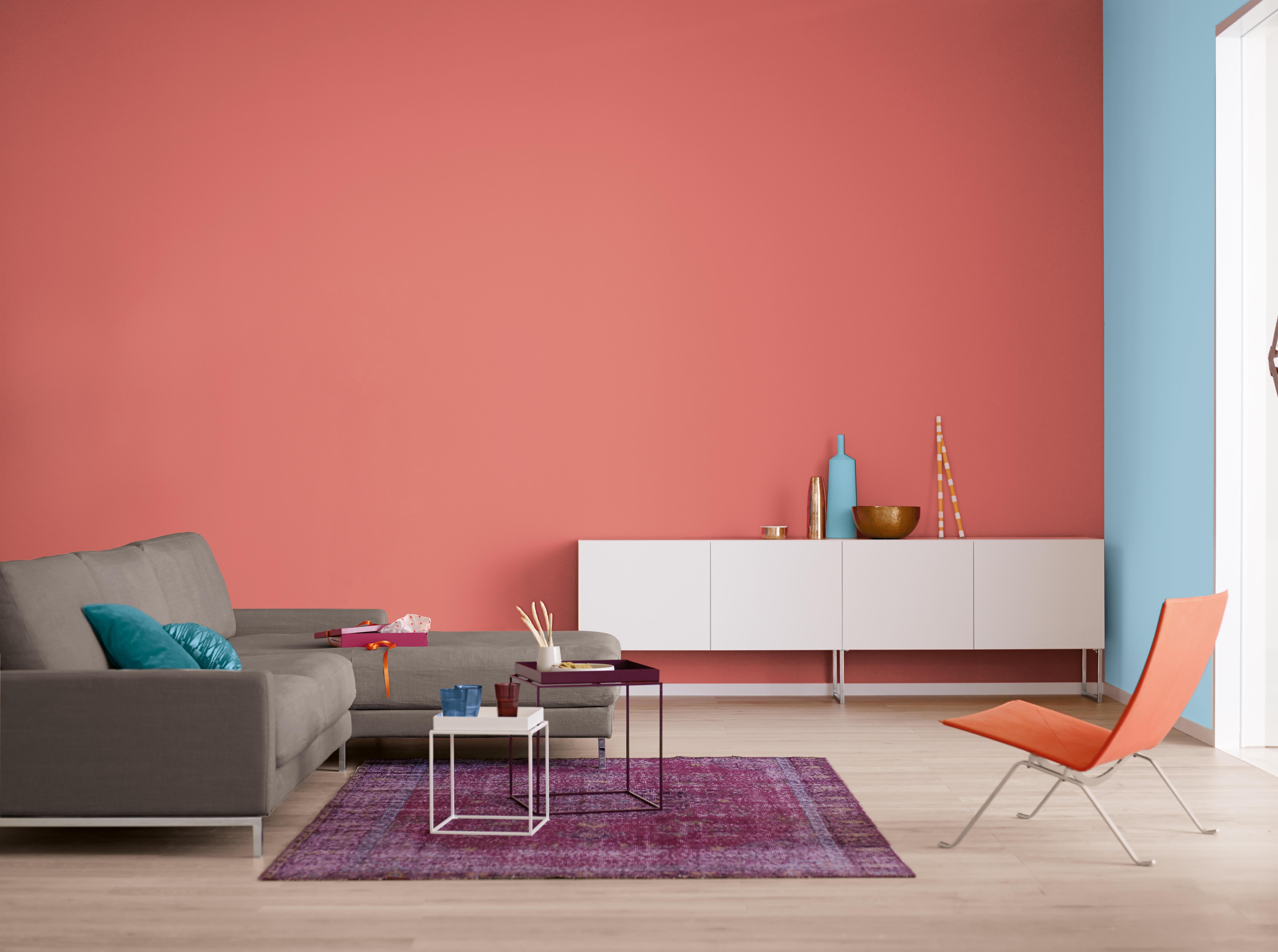 Modernes Wohnzimmer mit Beistelltischen, Sideboard, Sessel und Teppich vor rot und Himmelbalu gestrichenen Wänden.