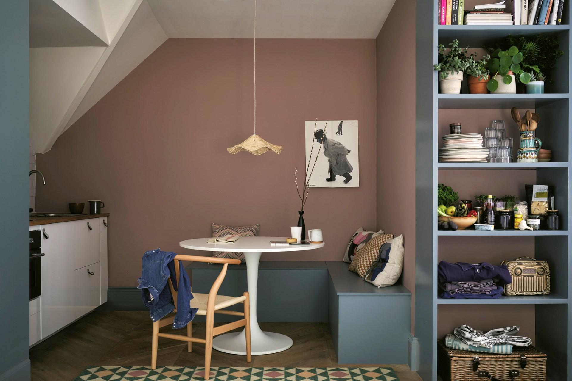 Essecke mit grauer Eckbank, Retrotisch und skandinavischem Stuhlklassiker vor dunkelrosa gestrichener Wand.