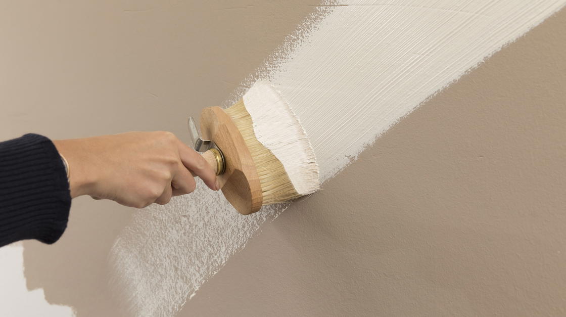 Hand mit Pinsel, die eine Wand mit Lehmfarbe streicht