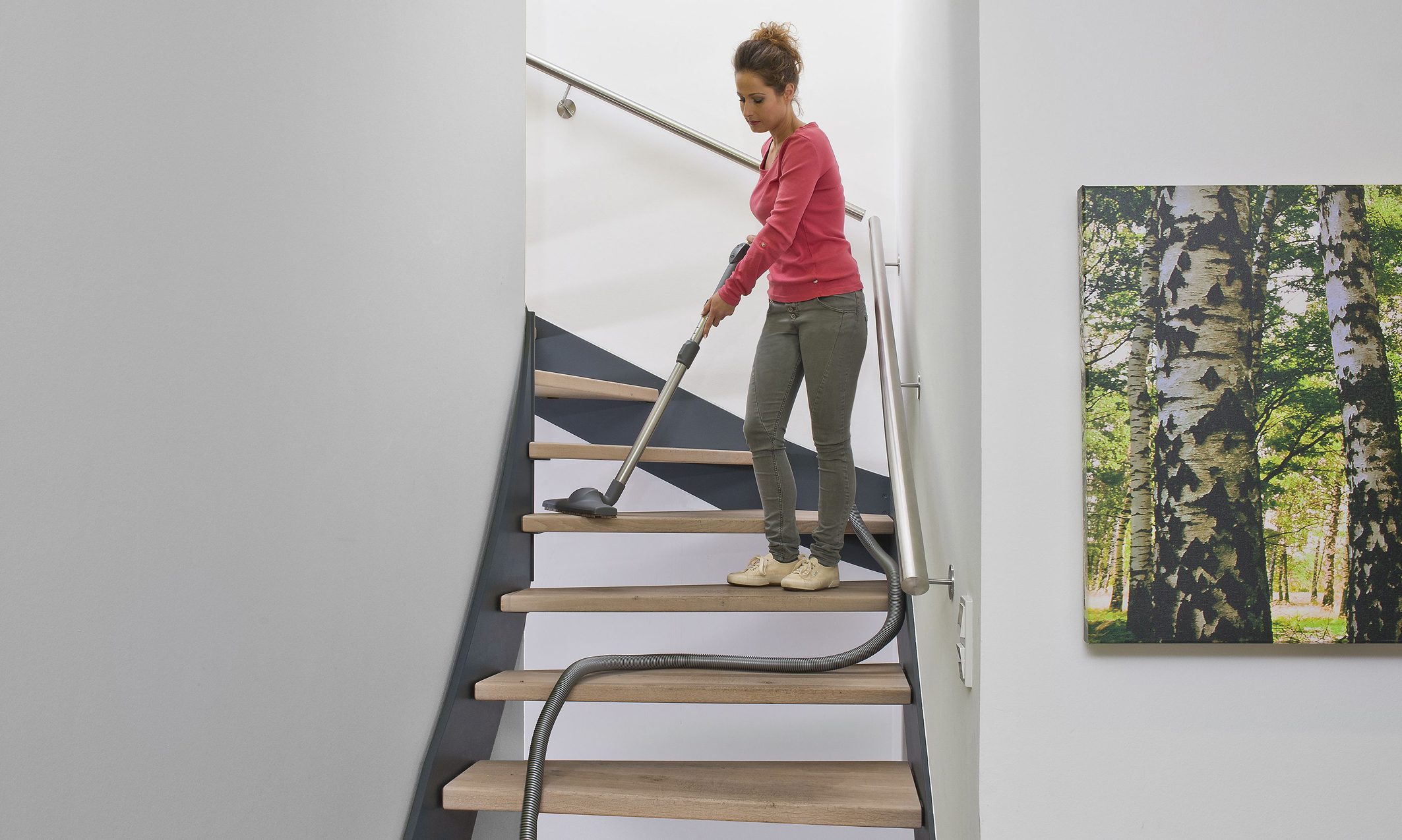 Frau saugt Treppe mit einer Staubsaugeranlage