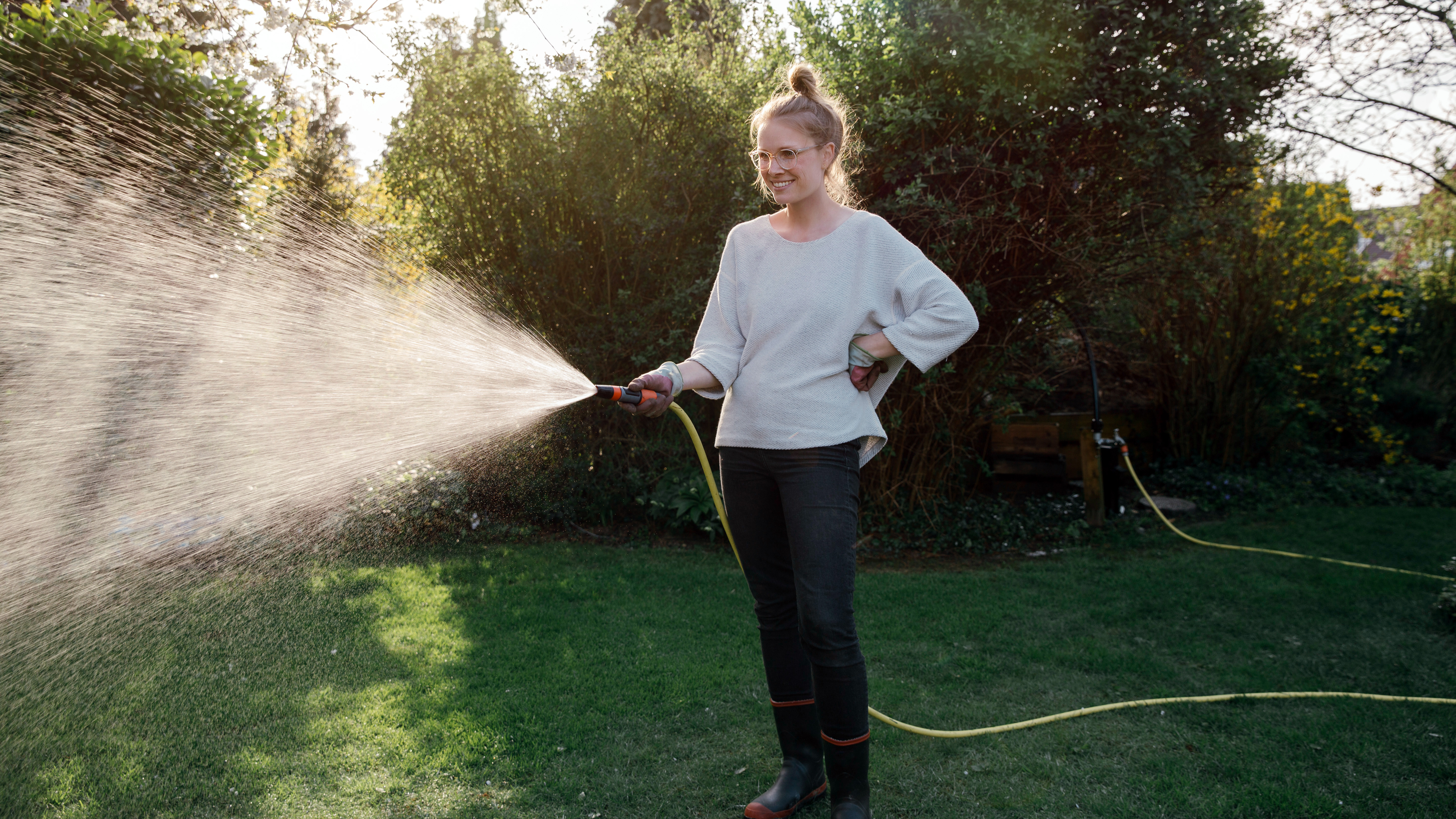Eine junge Frau gießt mit dem Gartenschlauch