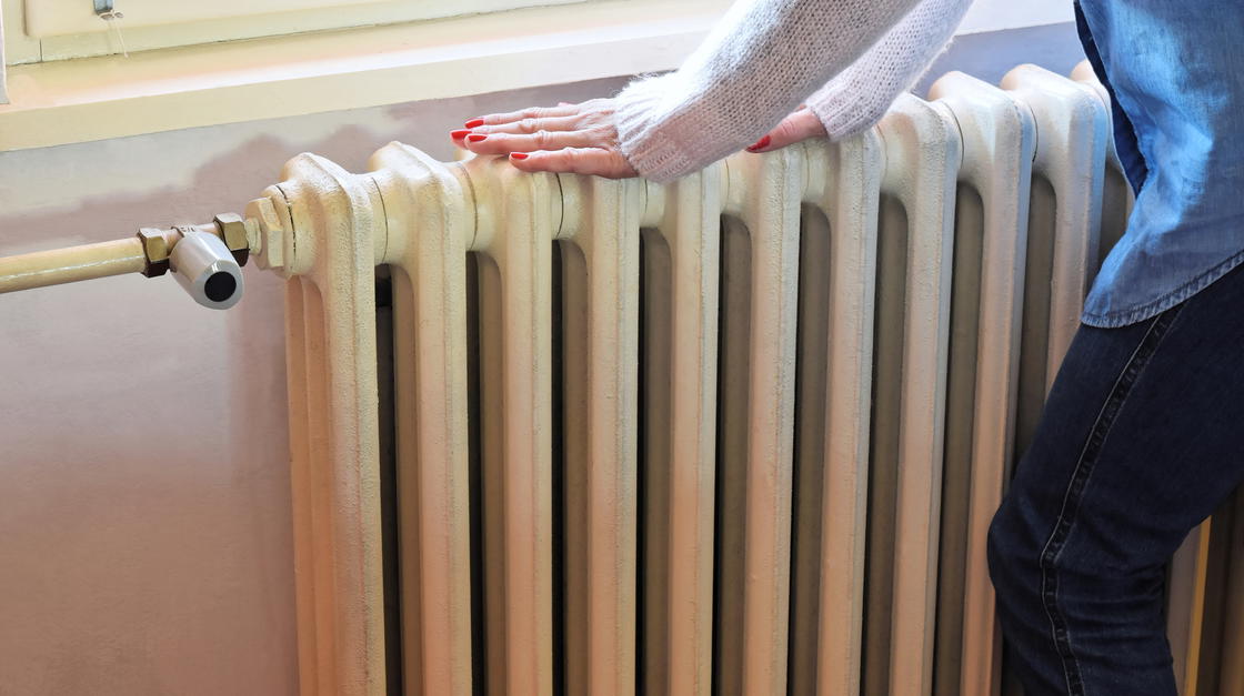 Frau prüft Temperatur bei einem alten Heizkörper.