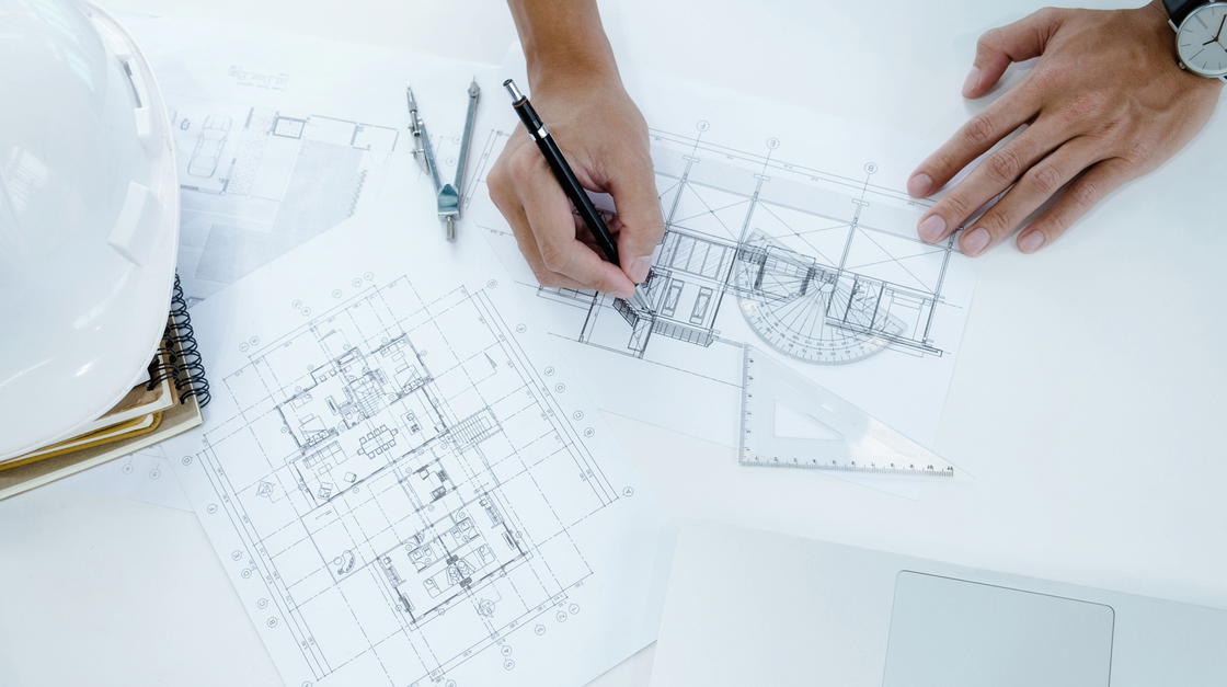 Architekt zeichnet etwas auf einem Bauplan ein.