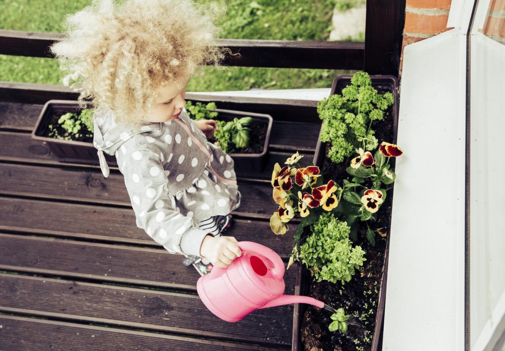 Kind gießt Blumen auf Balkon