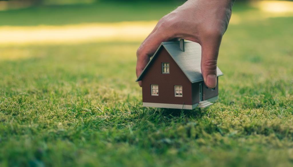 Hand hält Modellhaus über grüner Wiese