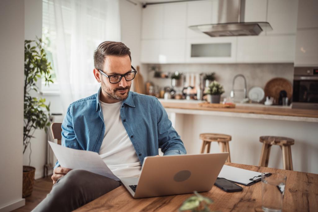 Mann sitzt mit Unterlagen und Laptop am Esstisch