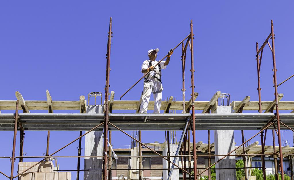 Arbeiter montiert vor blauem Himmel Gerüst auf einem Gebäude