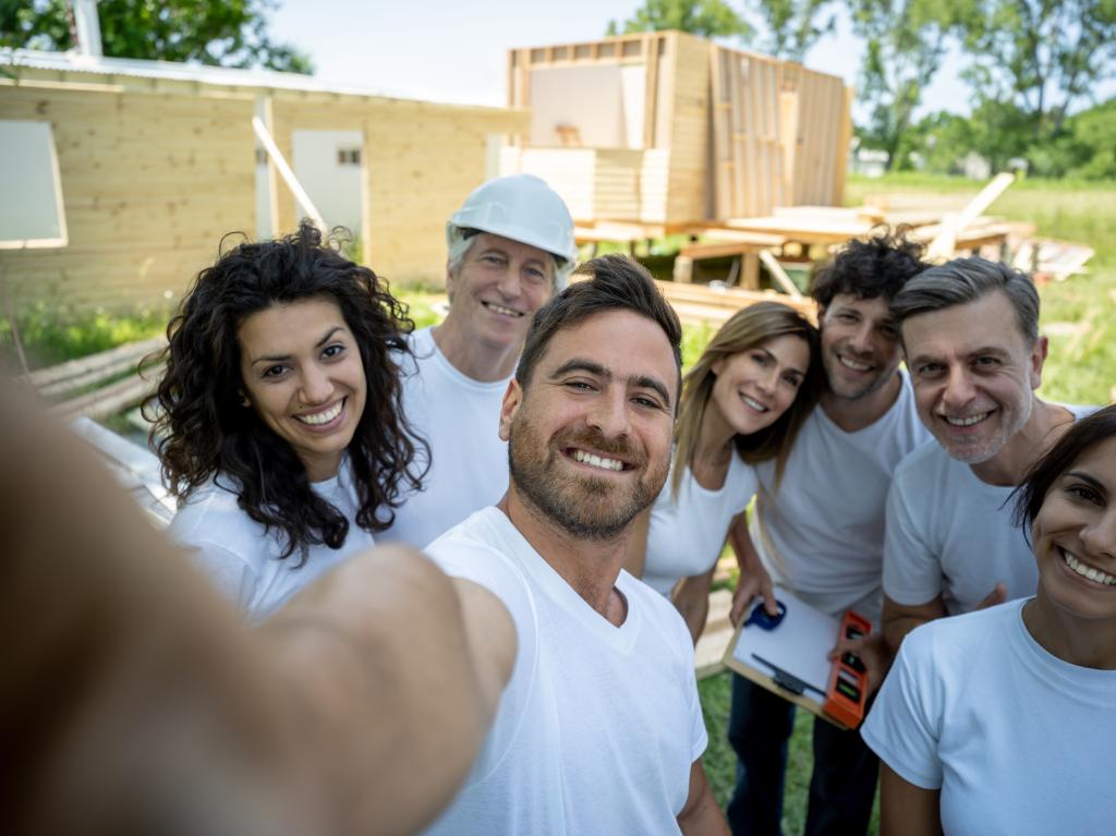 Eine Gruppe gemischten Alters auf einer Baustelle, die ein Selfie machen, lächeln vor der Kamera.