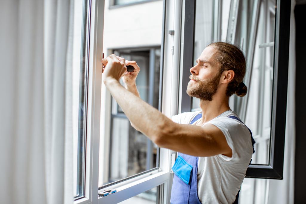 Mann baut ein Fenster von innen ein.