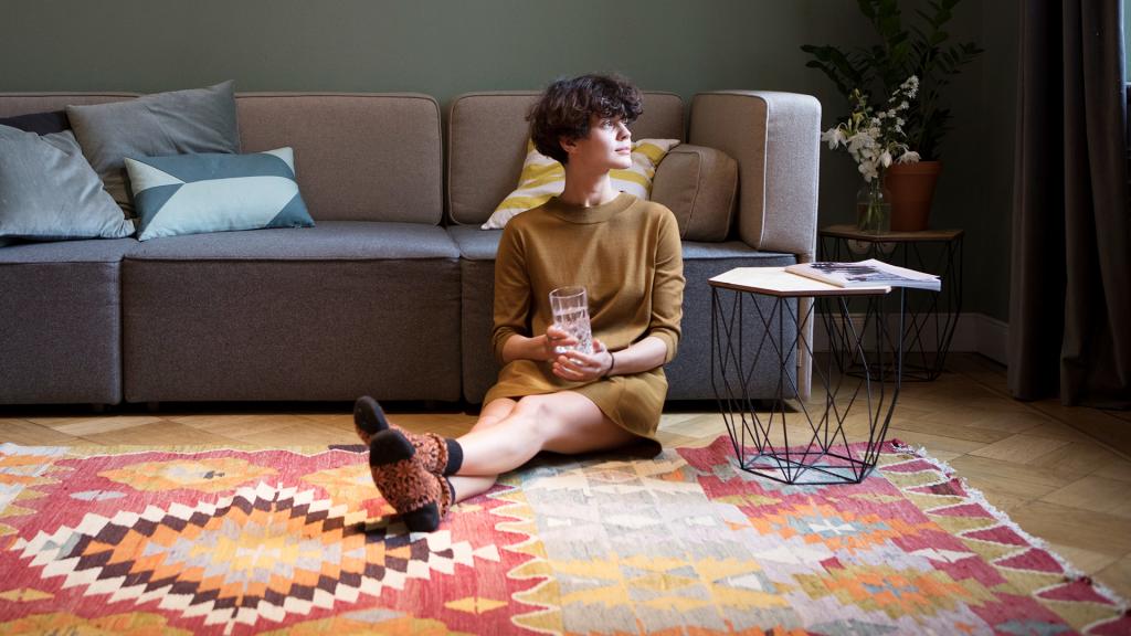 Junge Frau mit kurzen Haaren sitzt auf einem Teppich vor dem Sofa