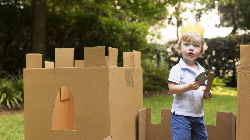 Junge steht in Burg aus Pappe im Garten
