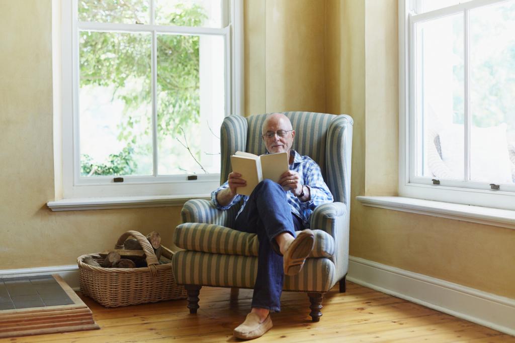 Älterer Mann sitzt in Sessel in Haus und liest ein Buch