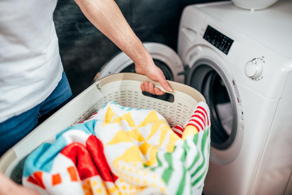 Frau trägt Wäschekorb mit Handtüchern zur Waschmaschine