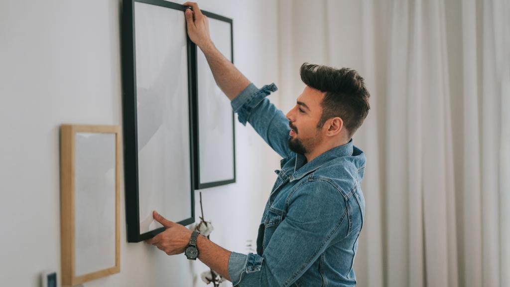 Ein Mann hängt Bilder in seiner Wohnung auf