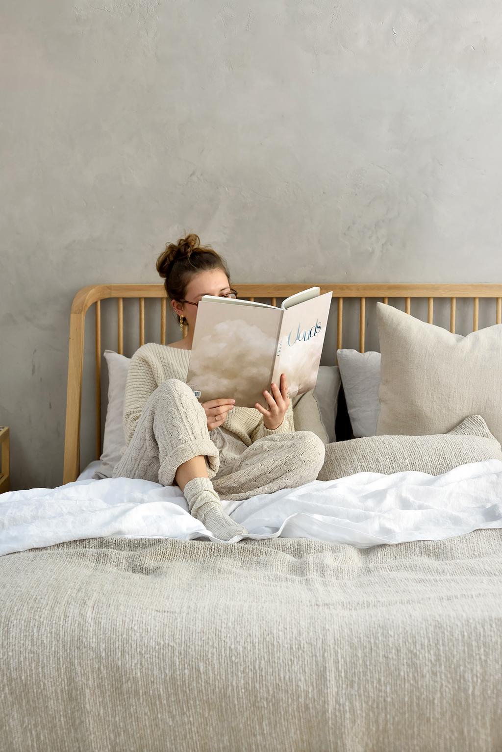 Frau liest gemütlich ein Buch auf einem Bett.