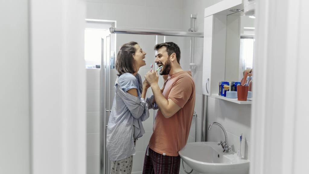 Junges Paar lacht beim Zähneputzen im Bad.