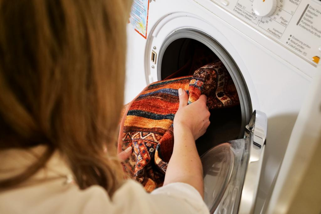 Frau legt waschbaren Teppich in Waschmaschine
