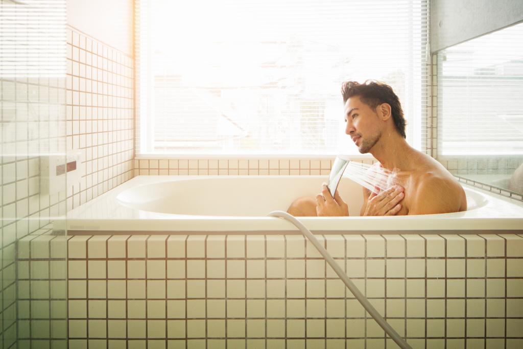 Mann mit Duschkopf in Badewanne
