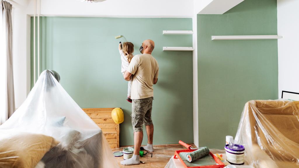 Vater und Tochter streichen gemeinsam eine Zimmerwand.