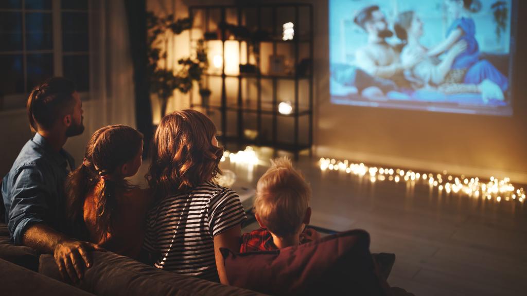 Eine Familie sitzt auf dem Sofa und guckt einen Film auf der Leinwand.