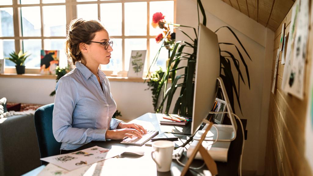 Frau mit Brille sitzt am Schreibtisch vor einem Computer.