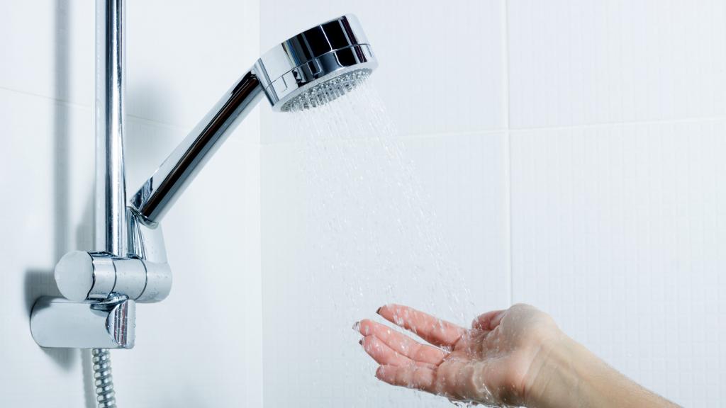 Frau hält Hand unter laufenden Wasserstrahl in der Dusche im Badezimmer