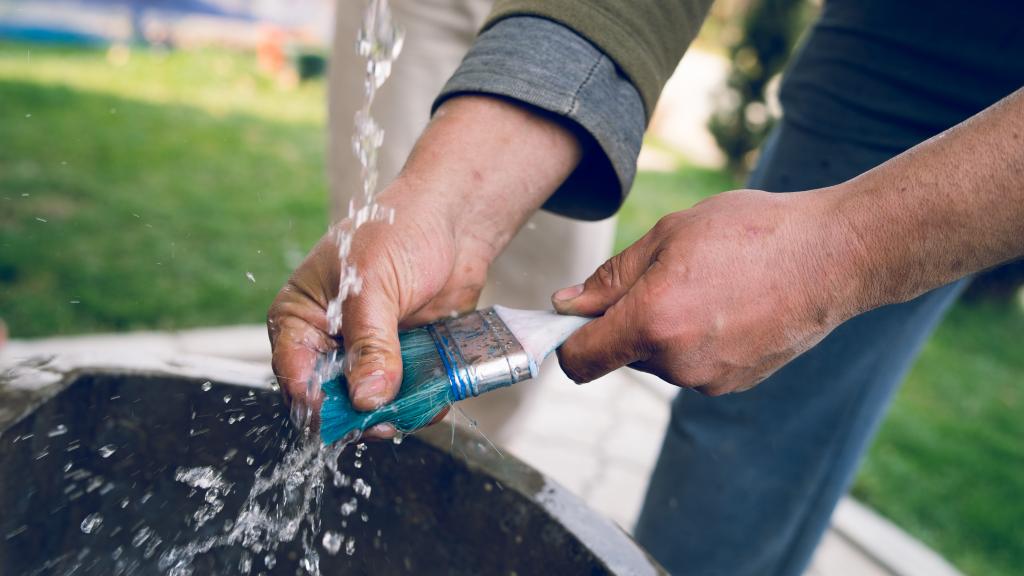 Mann säubert Pinsel unter Wasserstrahl im Garten