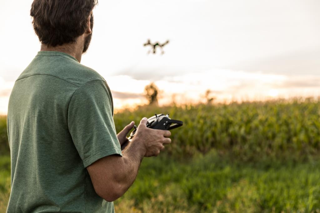 Mann fliegt Drohne über freiem Feld in der Abenddämmerung.