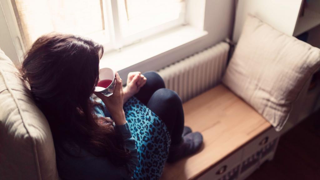 Eine Frau sitzt am Fenster und trinkt Tee.