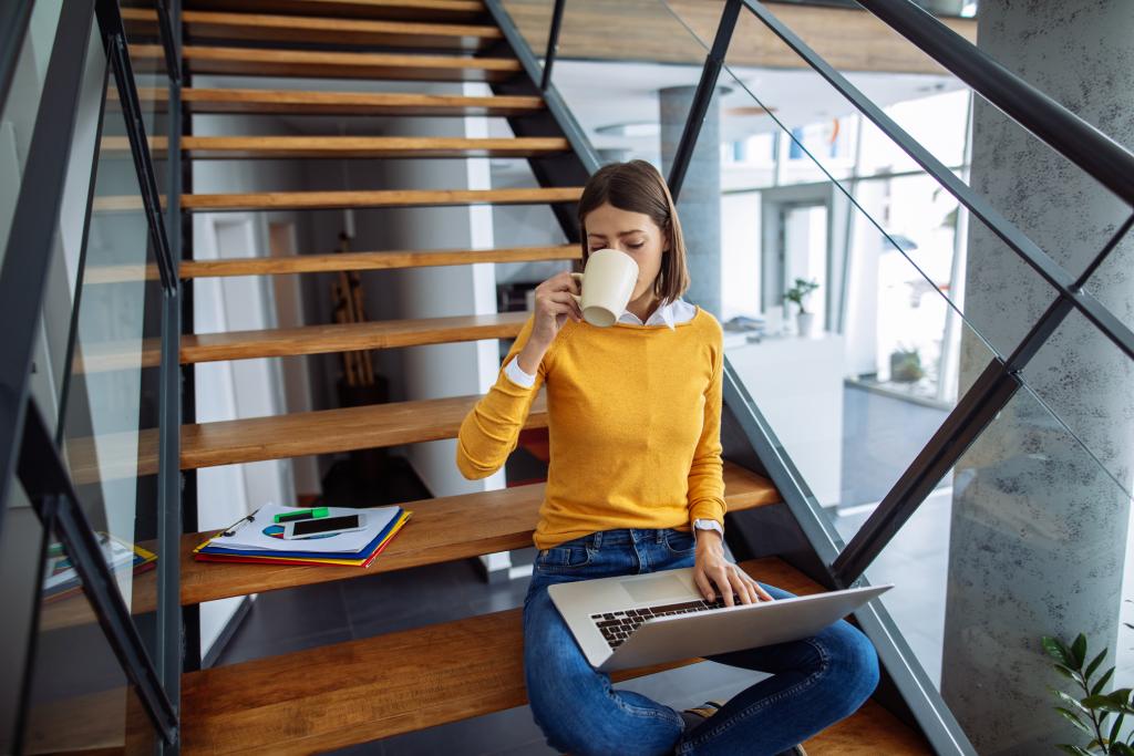 Frau mit Laptop und Kaffee sitzt auf Treppenstufen