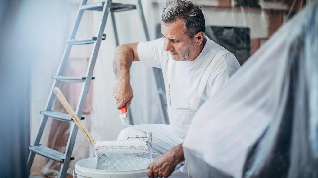 Maler streicht Farbrolle in Farbeimer aus