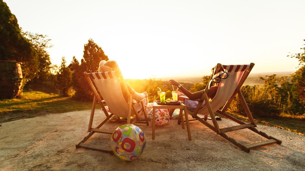 Paar liegt auf Liegestühlen im Garten und guckt Sonnenuntergang an