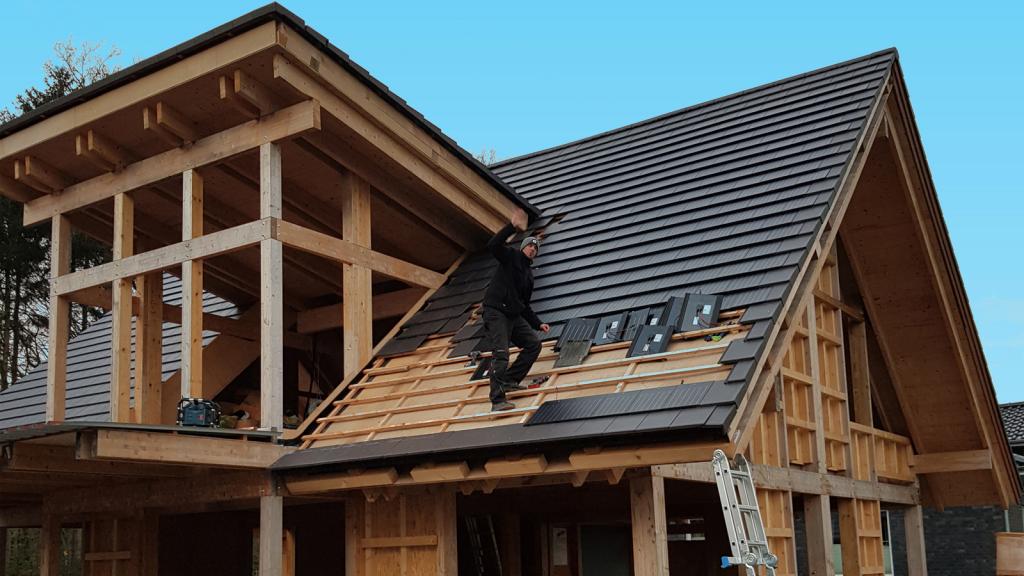 Mann deckt Dach mit Solardachziegeln ein.