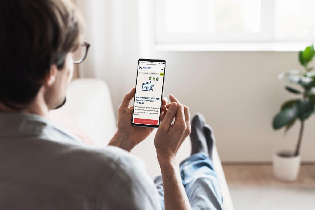 Mann liegt auf Sofa und macht Immobilienbewertung über Smartphone