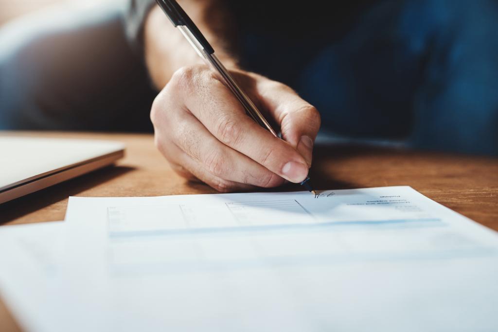 Hand mit Stift unterschreibt Vertrag