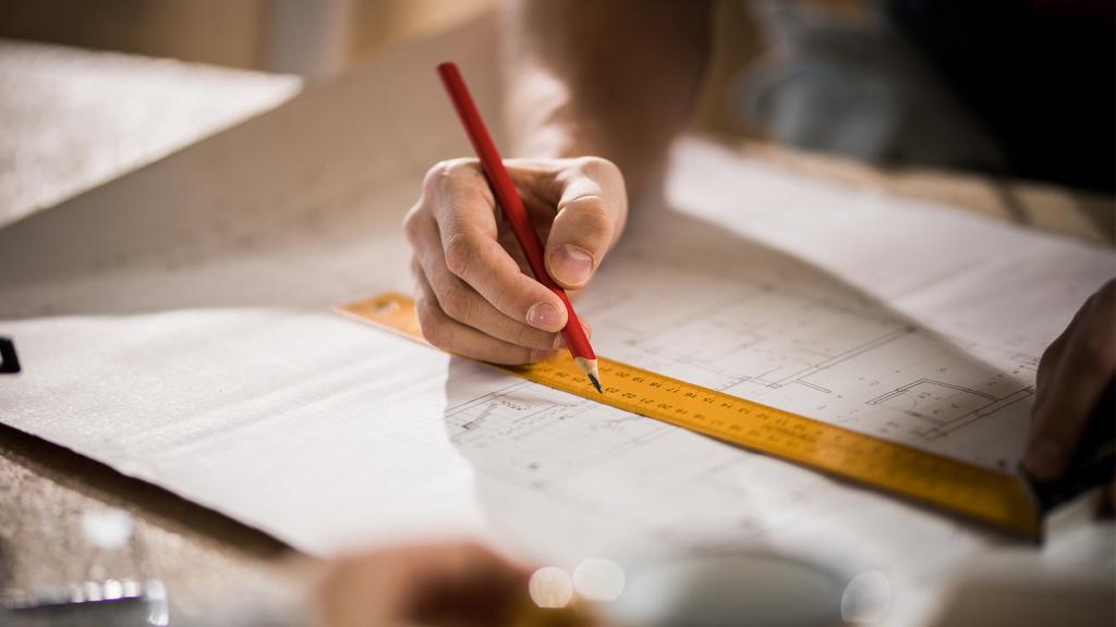 Hand zeichnet etwas mit Stift in Bauplan ein