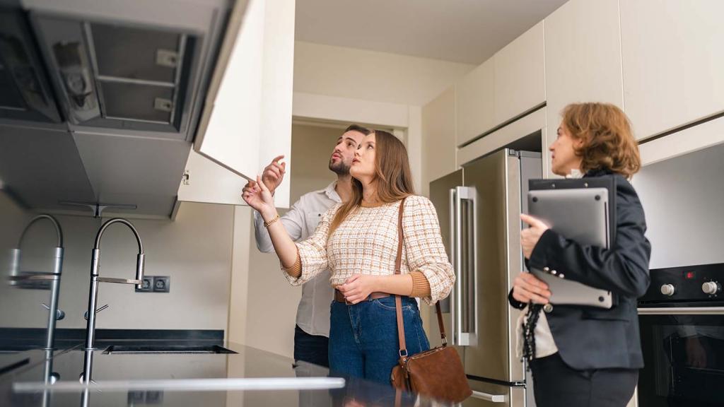 Paar schaut sich mit Makler Küche in Wohnung an