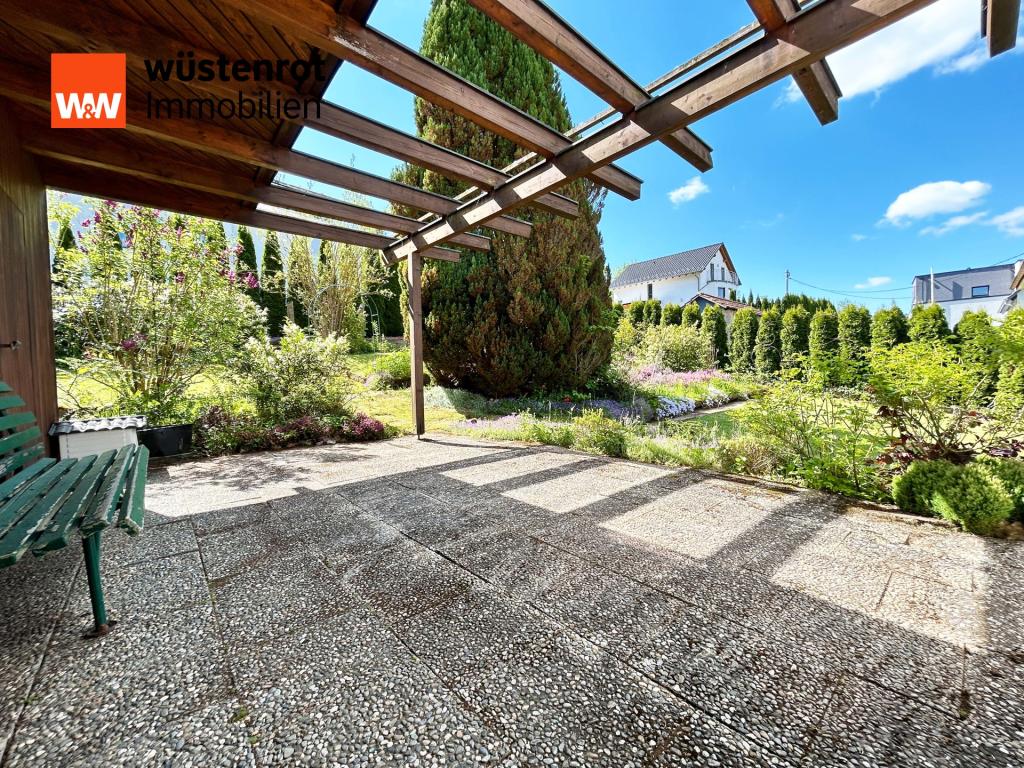Hier wirft die Pergola Schattenmuster, während der Garten in voller Blüte schweigt – ein Platz für Gespräche und Kaffee in der Morgensonne